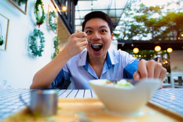 カメラ目線の朝食に穀物を食べるアジアの空腹の男。