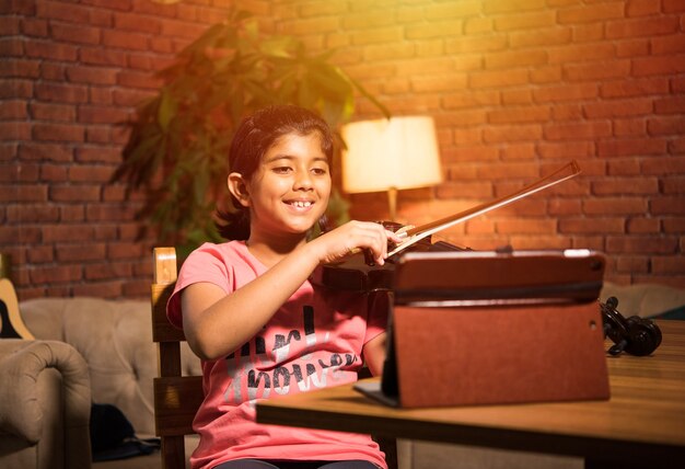 Photo asian indian child learning music or musical instrument online using laptop computer or tablet at home, persuing hobby