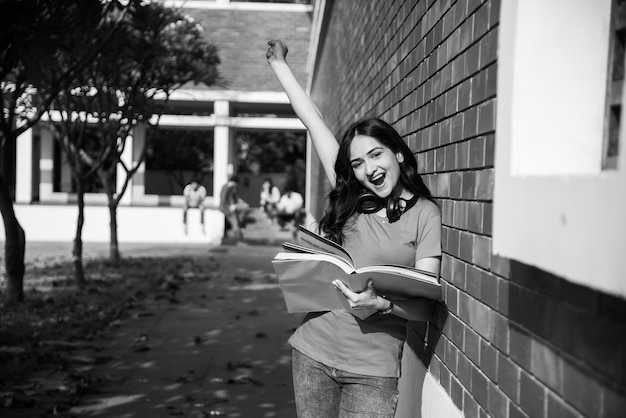 Asian Indian college student in focus working on laptop or reading book while other classmates in the background, outdoor picture in university campus