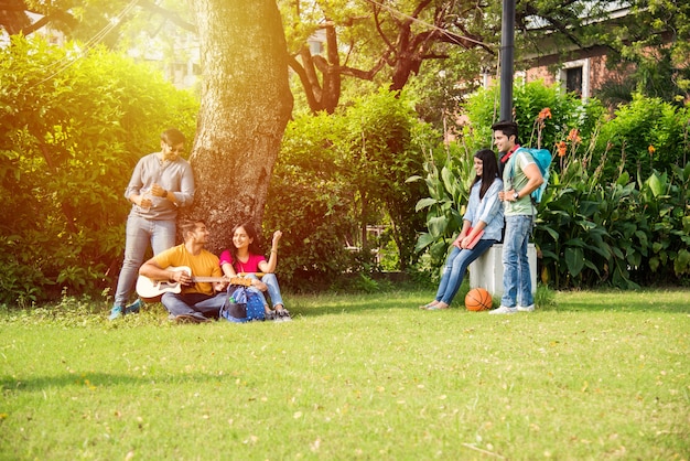 Asian Indian college students playing music with guitar while sitting in campus on stairs or over lawn