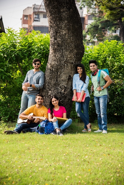 Азиатские индийские студенты колледжа играют на гитаре, сидя в кампусе на лестнице или на лужайке