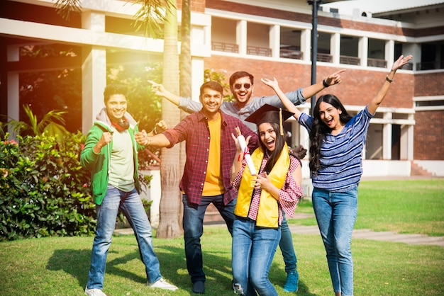 Studenti universitari indiani asiatici ricevono un certificato di laurea mentre gli amici festeggiano nel campus universitario all'aperto