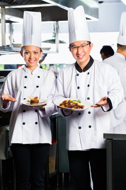 Азиатский индонезийский шеф-повар вместе с другими поварами в ресторане или отеле готовит на коммерческой кухне, готовит завершающее блюдо или тарелку