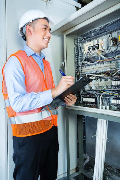 Asian Indonesian Technician or electrician making function test on breaker box or switchbox with power lines on construction site or in factory for acceptance