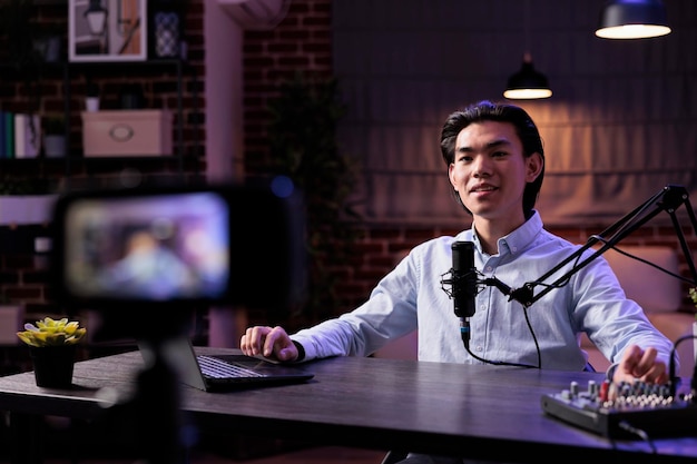Asian influencer livestreaming talk show on social media\
channel, using sound equipment and laptop at studio station.\
filming online video blog with podcast production, recording vlog\
content.
