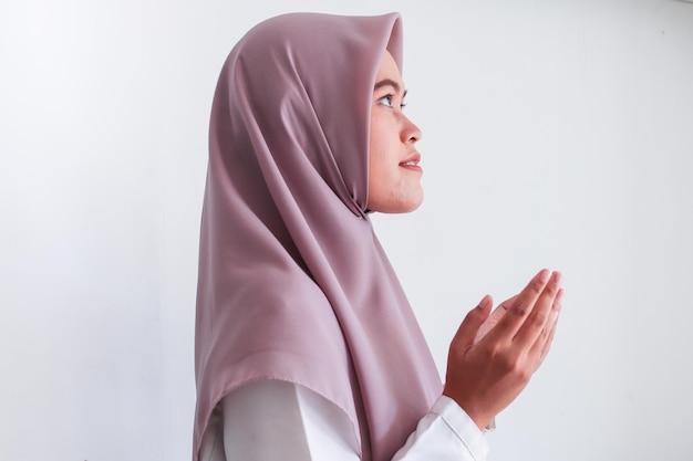 Asian Islam Muslim woman in headscarf and hijab prays with her hands up in air with smile face Indonesian woman Religion praying concept isolated on grey background