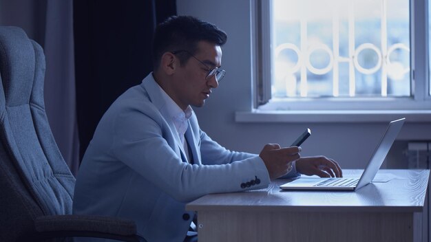 Asian Kazakh businessman in a suit and glasses with a laptop computer in the office speaks by mobile phone, solves business issues, negotiates a deal.