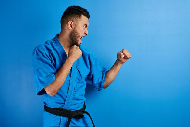 Asian Kazakh karate fighter in kimono uniform is combat on blue background with copy space isolated