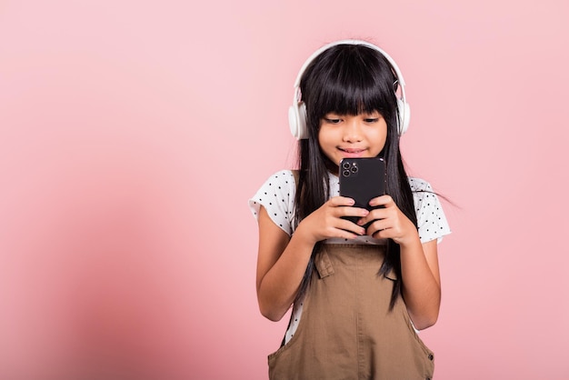 Asian kid 10 years enjoying listening music from mobile phone wear wireless headset