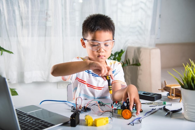 asian kid boy assembling the arduino robot car homework project at home