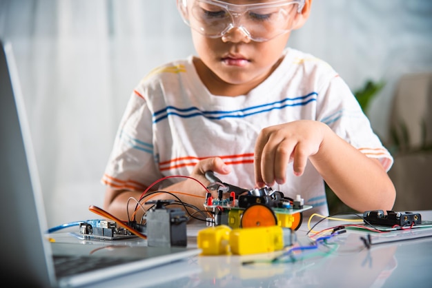 Asian kid boy assembling the Arduino robot car homework project at home