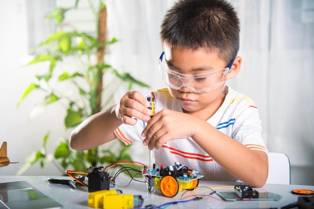 Asian kid boy assembling the Arduino robot car homework project at home