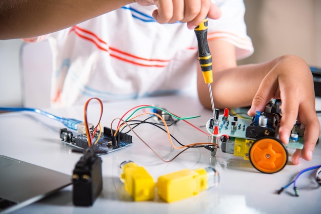 Asian kid boy assembling the Arduino robot car homework project at home