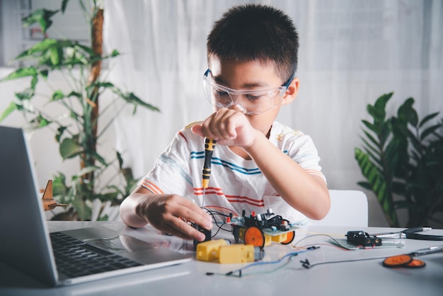 Asian kid boy assembling the Arduino robot car homework project at home