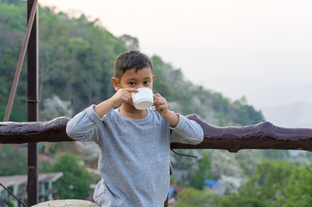 아시아 꼬마 소년 유리에서 물을 마시고있다. 산 전망 배경으로
