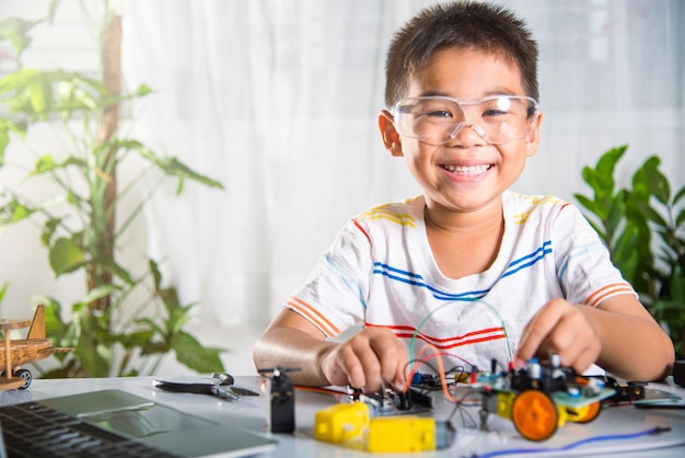 Photo asian kid boy plugging energy and signal cable to sensor chip with arduino robot car
