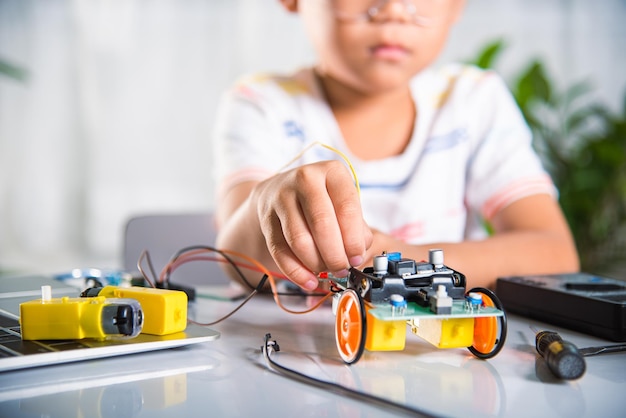 Asian kid boy plugging energy and signal cable to sensor chip with Arduino robot car