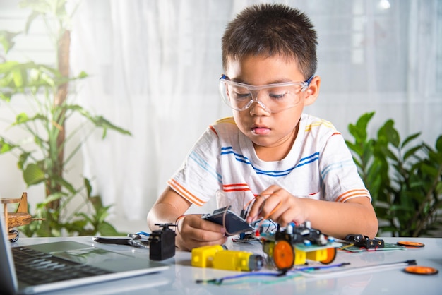 Photo asian kid boy plugging energy and signal cable to sensor chip with arduino robot car