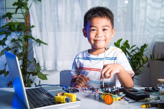 Asian kid boy plugging energy and signal cable to sensor chip with Arduino robot car