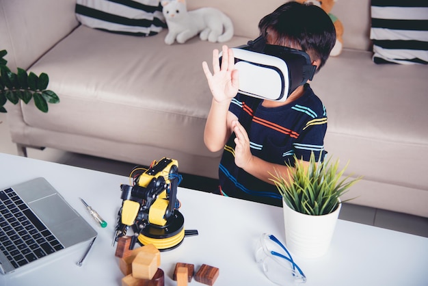 Asian kid boy using VR glasses on robotic arm in workshop