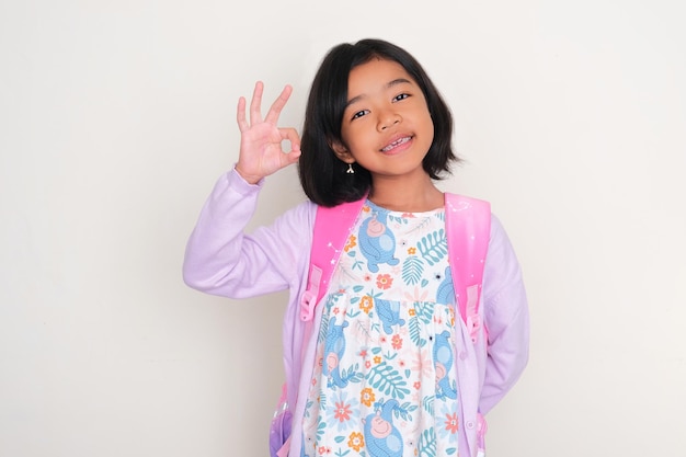 Asian kid carrying a school bag showing happy expression and give OK sign