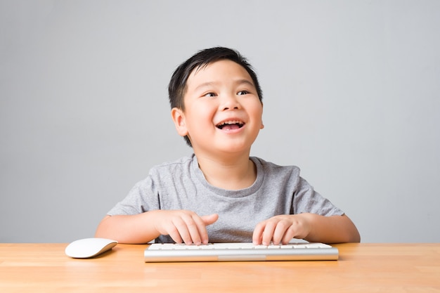写真 アジアの子供/幸せな子供は笑顔でキーボードとマウスを使ってオンラインレッスンを勉強します。オンライン学習と自己学習の概念。