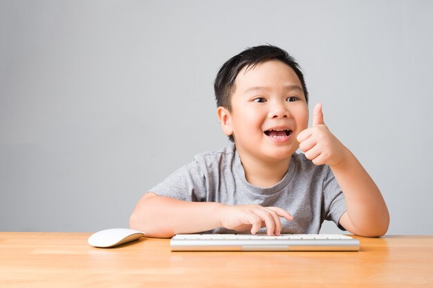 Foto bambino asiatico / bambino felice che sorride e utilizza tastiera e mouse, d'accordo con le lezioni online di studio. apprendimento online e concetto di studio individuale.