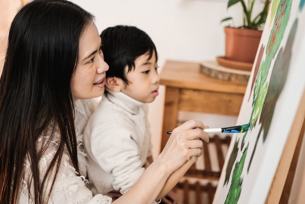 Asian kid and mom painting on canvas during art class at home - focus on woman eye