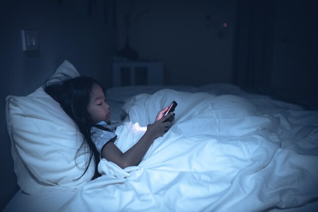 夜ベッドでスマートフォンでゲームをしているアジアの子供The girl Addict social media