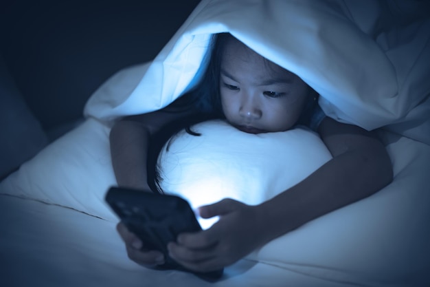 夜ベッドでスマートフォンでゲームをしているアジアの子供The girl Addict social media