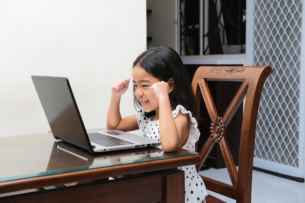 Asian kid showing excited expression with both fist clenched when looking to her laptop