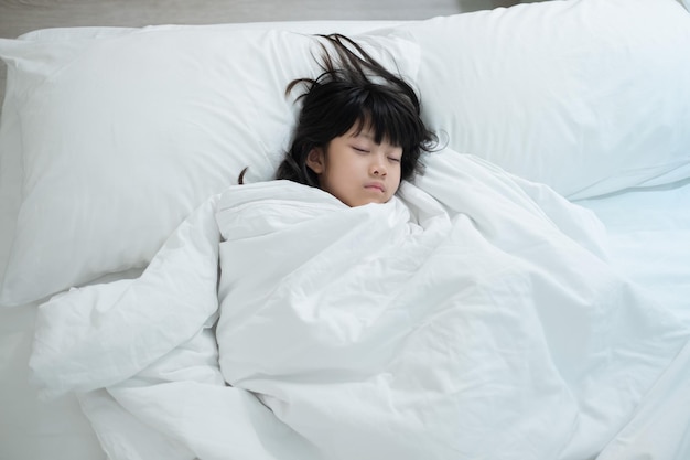 アジアの子供はベッドの病気の子供で寝る