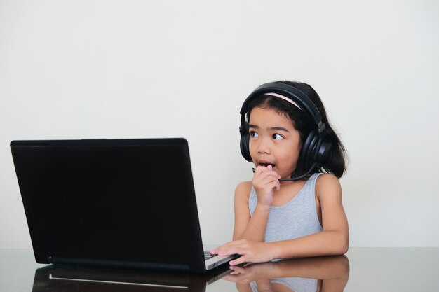 Asian kid talking using headset in front of laptop during her school online class