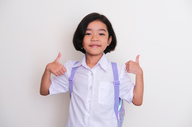 Asian kid wearing school uniform and backpack smiling and give two thumb up