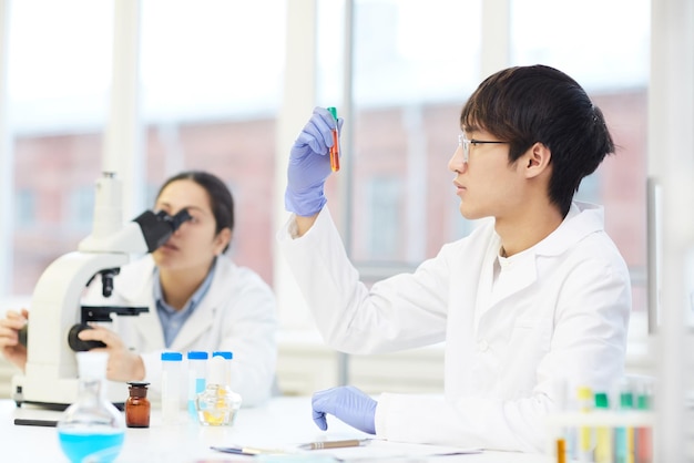 Asian lab employee looking at liquid in test tube