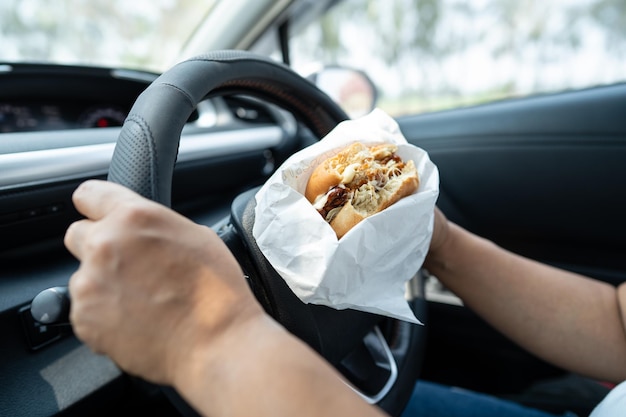 ハンバーガーとフライドポテトを車で食べるアジア人女性が危険で事故を起こす