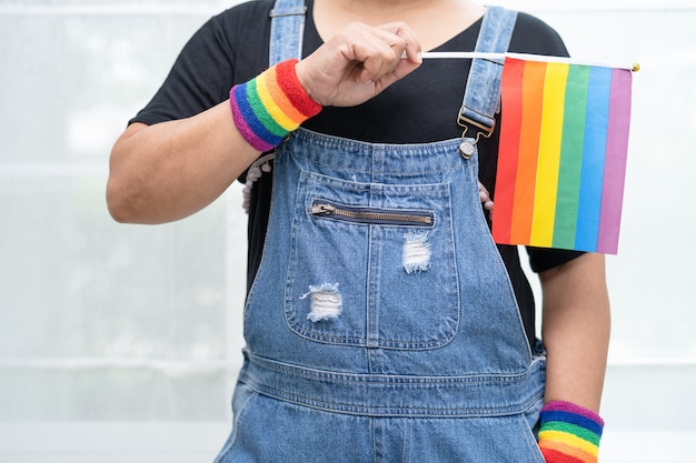 La signora asiatica che tiene in mano il simbolo della bandiera color arcobaleno del mese dell'orgoglio lgbt celebra l'annuale a giugno