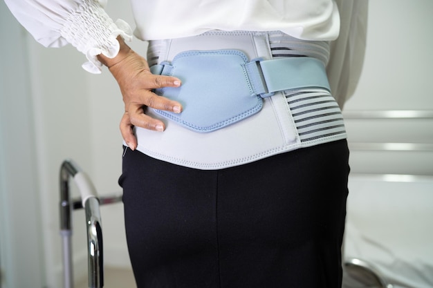 Paziente di signora asiatica che indossa cintura di supporto per il dolore alla schiena per lombare ortopedico con camminatore