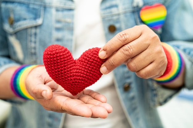 Foto donna asiatica che indossa braccialetti con bandiera arcobaleno e tiene un cuore rosso simbolo del mese dell'orgoglio lgbt celebra annualmente a giugno il social dei diritti umani dei gay lesbiche bisessuali transgender