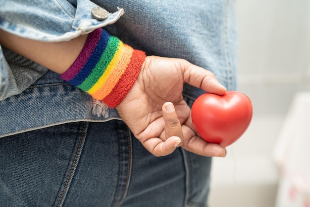 Asian lady wearing rainbow flag wristbands and hold red heart symbol of LGBT pride month celebrate annual in June social of gay lesbian bisexual transgender human rights