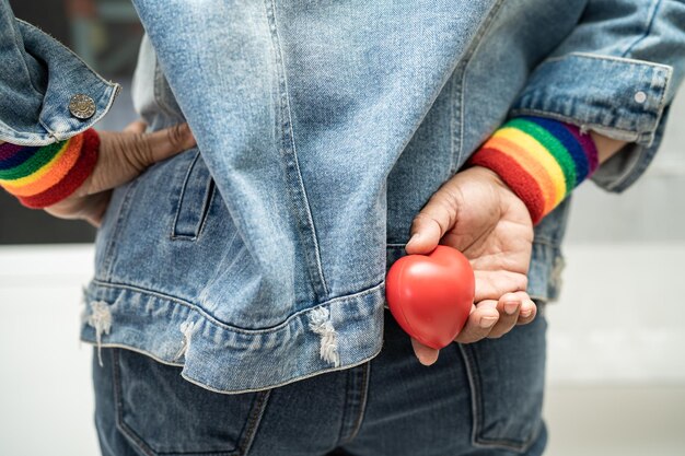 무지개 깃발 팔찌를 착용하고 LGBT 프라이드의 달의 붉은 심장 상징을 들고 있는 아시아 여성은 게이 레즈비언 양성애자 트랜스젠더 인권의 사회에서 매년 6월을 축하합니다