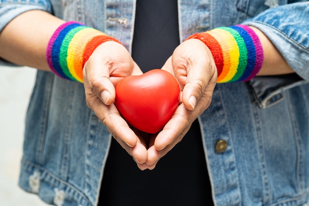 무지개 팔찌를 착용하고 LGBT 자부심 달의 상징, 붉은 마음을 잡고 아시아 아가씨.