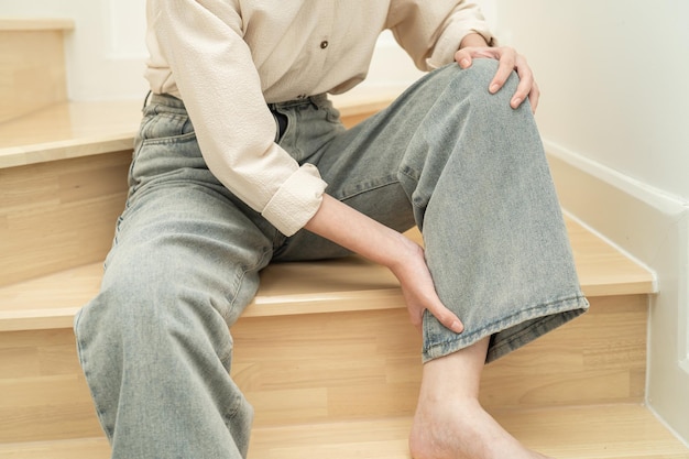 Asian lady woman touch and feel pain her knee on the stairs at\
home healthy medical concept