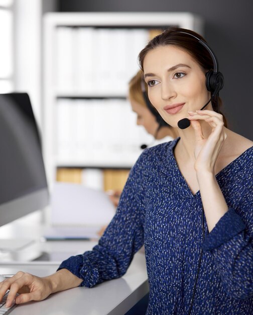 Asian or Latin american businesswoman talking by headset while sitting in office. Call center and diverse people group in business.