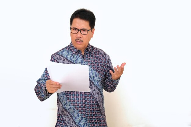 Photo asian lecturer holding his student assignment paper with unhappy facial expression