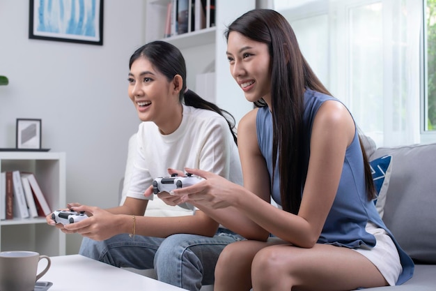 Asian lesbian lgbt women couple play video games at home females having funny happy moment together on sofa in living room