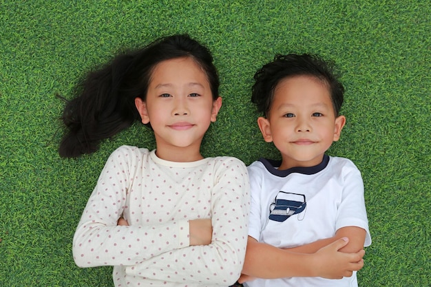 Азиатский маленький мальчик и девочка лежат на зеленом фоне травы вместе с камерой