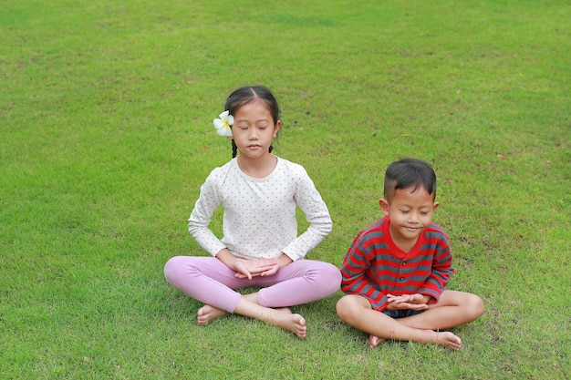 Asian little boy and girl child practicing mindfulness meditation sitting on lawn in the garden Peaceful concept