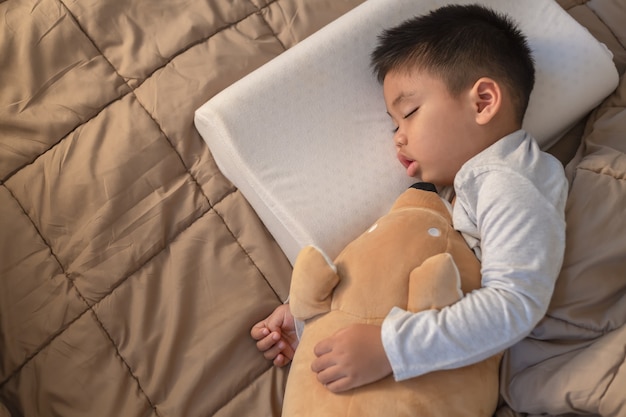 Asian little boy Sleeping on a warm brown fabric on the bed, holding a teddy.