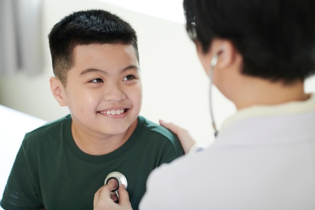 Asian little boy smiling to doctor while she examining his heartbeat with stethoscope